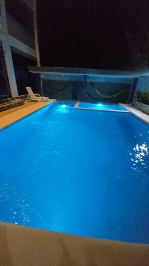 Una piscina con bordo piastrellato e una poltrona da relax bianca.