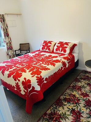 A bed with a red and white floral bedspread, a chair, and a window with floral curtains. - Cute cottage in Grey Lynn (Auckland)