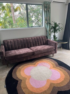 A brown sofa in a room with a large window, a round rug, and a potted plant. - Cute cottage in Grey Lynn (Auckland)