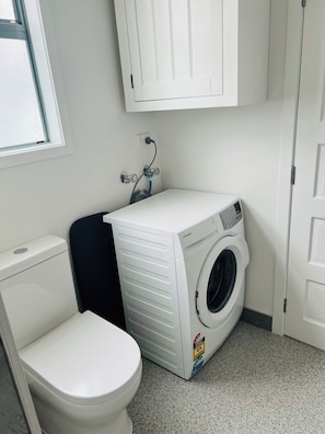 A compact laundry room with a washing machine, a dryer, and a toilet. - Cute cottage in Grey Lynn (Auckland)