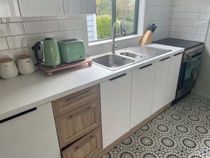 A kitchen with a sink, two green kettles, a knife block, and patterned floor tiles. - Cute cottage in Grey Lynn (Auckland)