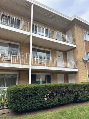 En flervåningsbostadsbyggnad med balkonger, en fasad av tegel och en välskött häck framför.