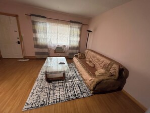 Ein Wohnzimmer mit einer Couch, einem Couchtisch, einem gemusterten Teppich, einer Tür und einem Fenster mit Vorhängen.