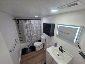 A bathroom with a shower, toilet, sink, and a mirror with a light. - Cozy Home Away From Home |Inviting 2 Bedroom! (Saratoga Springs)