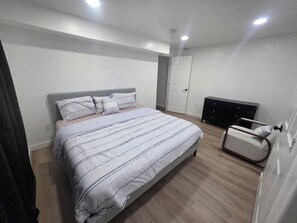 A bedroom with a bed, a bedside table, a chair, and a wardrobe. - Cozy Home Away From Home |Inviting 2 Bedroom! (Saratoga Springs)
