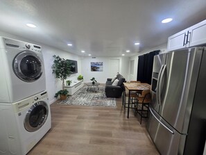 A compact kitchen with a washing machine, a refrigerator, a dining area with a table and chairs, and a seating area with a sofa. - Cozy Home Away From Home |Inviting 2 Bedroom! (Saratoga Springs)