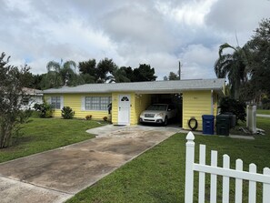 A single-story yellow house with a garage, a white picket fence, and a driveway leading to the garage. - "The Yellowbelle" Pinecraft N. - Sarasota 2b/1b Private Apartment w/ Shared Wall (Sarasota)