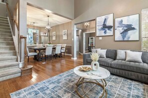 Ein geräumiges Wohnzimmer mit grauem Sofa, einem Essbereich mit Tisch und Stühlen sowie einer Treppe mit Holzwertungen.