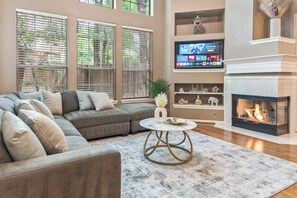 Ein Wohnzimmer mit einem Ecksofa, einem Kamin und einem an der Wand befestigten Fernseher.