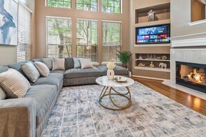 Ein Wohnzimmer mit einem Ecksofa, einem runden Couchtisch, einem Kamin und einem an der Wand montierten Fernseher.