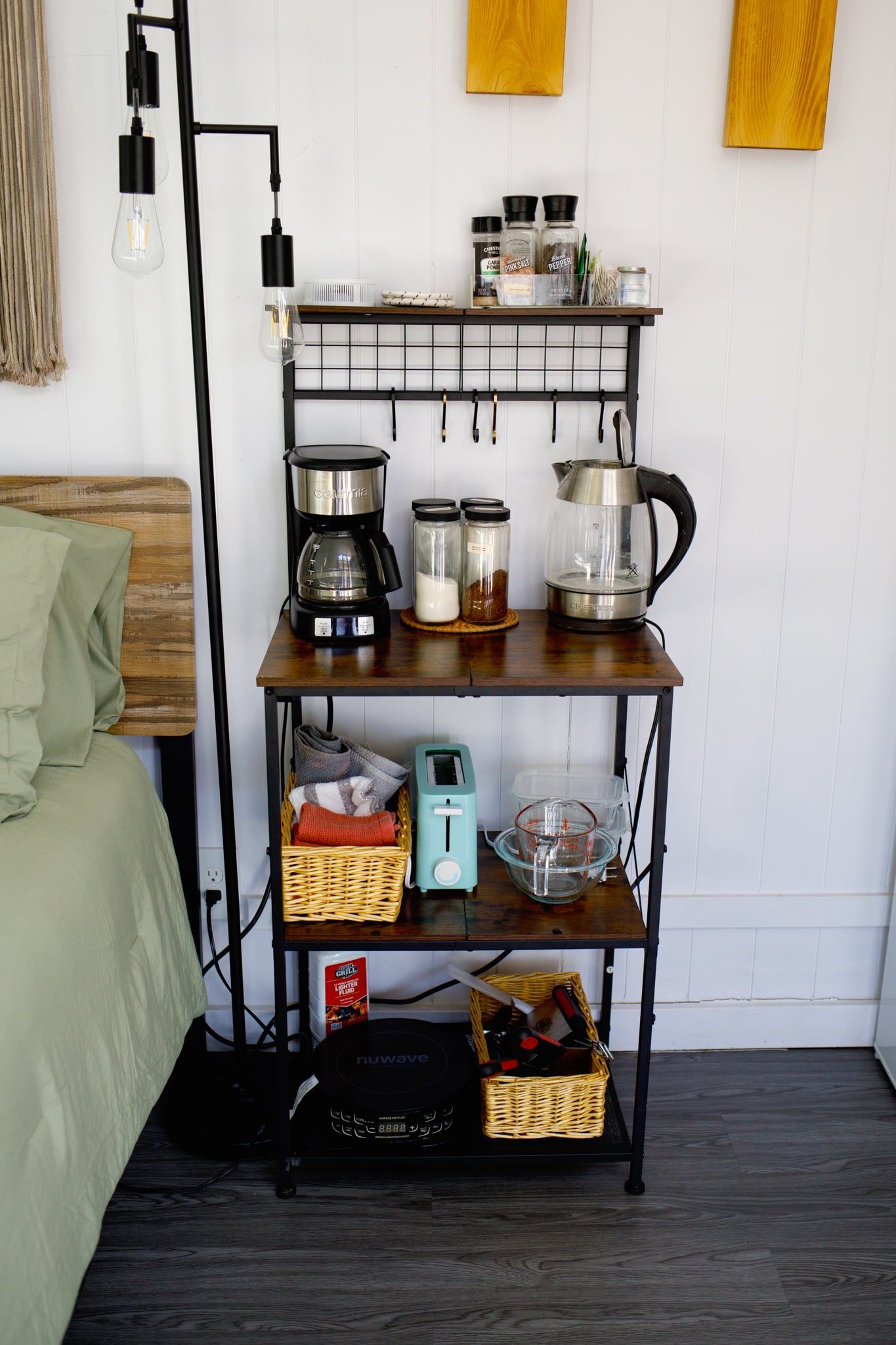 A kitchen area with a coffee maker, kettle, and various containers on a shelf.