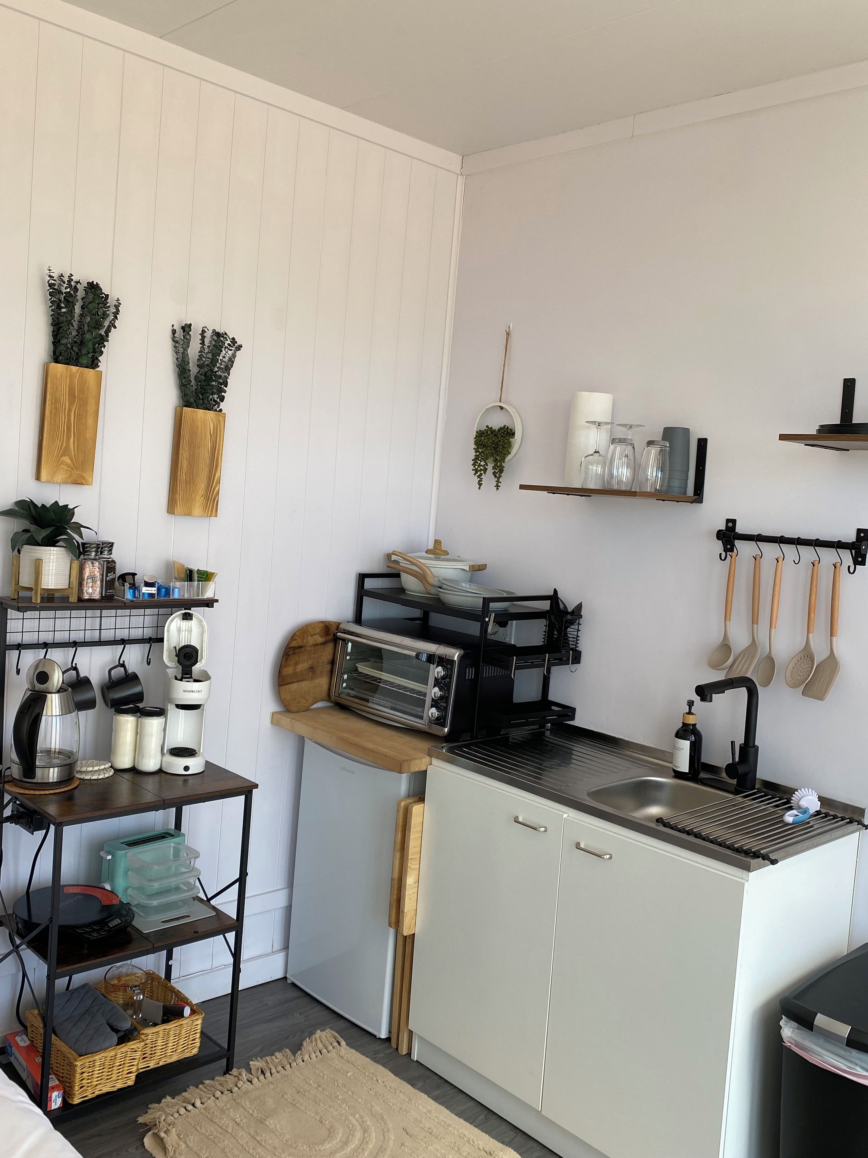 A compact kitchen with white cabinets, a wooden countertop, a built-in toaster, and a hanging pot rack.