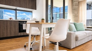 A modern kitchen with a dining area, a sofa, and a large window offering a city view. - Stylish Apt | King Bed, Balcony, Free Car Park & Indoor Swimming Pool (Docklands)