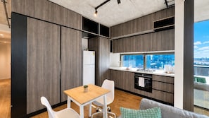A modern kitchen with a built-in oven, a dining area with a table and chairs, and a large window offering a city view. - Stylish Apt | King Bed, Balcony, Free Car Park & Indoor Swimming Pool (Docklands)