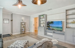 Ein Wohnzimmer mit Flachbildfernseher, Holzboden, Sofa, Couchtisch und Bücherregal.