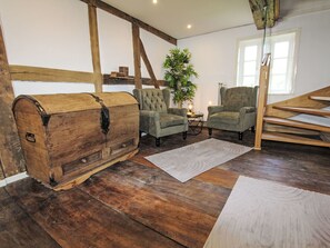 Un intérieur rustique avec une malle en bois, deux fauteuils, une plante en pot et une fenêtre.