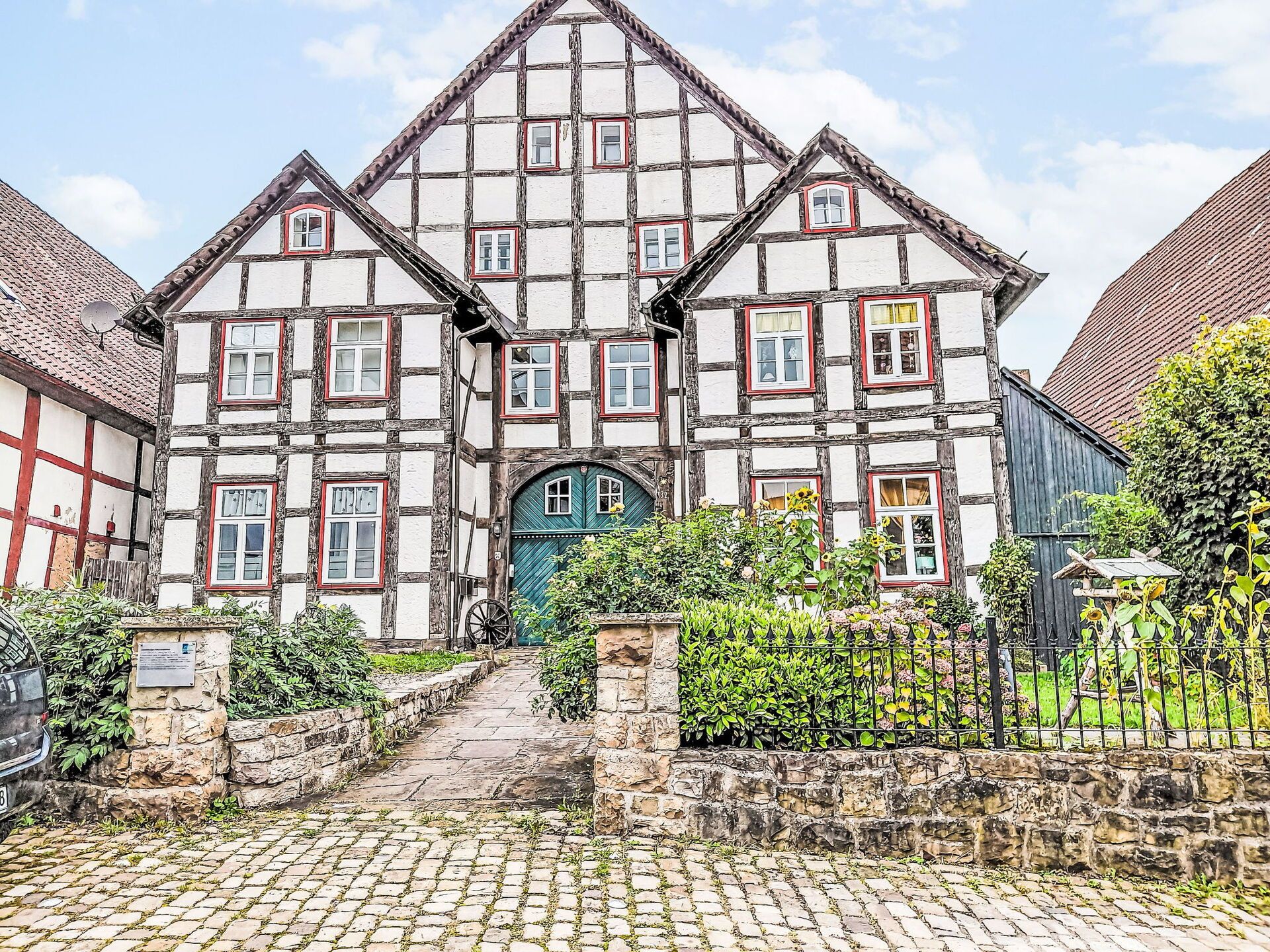 A traditional half-timbered house with a central entrance, stone walls, and a cobblestone pathway leading to the door.