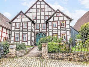 Ein traditionelles Fachwerkhäuschen mit einem zentralen Eingang, Steinmauern und einem Kopfsteinpflasterweg, der zur Tür führt.