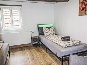 Ein Einzelbett mit Kopfteil, ein Nachttisch und ein Fenster mit Jalousien.