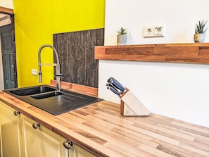 Una cocina con un lavamanos negro, encimera de madera y un bloque de cuchillos.