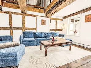 Ein Zimmer mit freiliegenden Holzbalken, einem blauen Sofagarnitur, einem Holztisch und einem großen Fenster mit Blick.