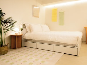 Een slaapkamer met een bed, nachtkastje, lamp, potplant en een spiegel aan de muur.