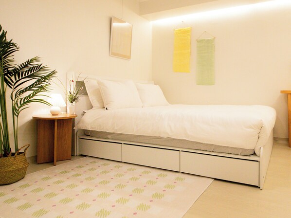 Een slaapkamer met een bed, nachtkastje, lamp, potplant en een spiegel aan de muur.