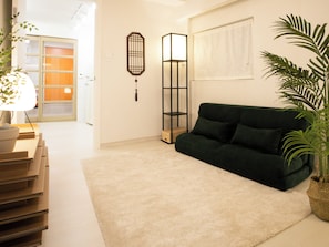 Ein Wohnzimmer mit einem dunkelgrünen Sofa, einer stehenden Stehlampe und einem Blumentopf.