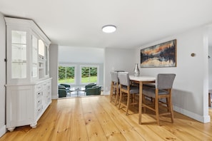 A dining area with a wooden table and chairs, a white cabinet, and a painting on the wall. - Wood Pond Lodge - Single Fam Oasis on 3 acres (Middlesex)