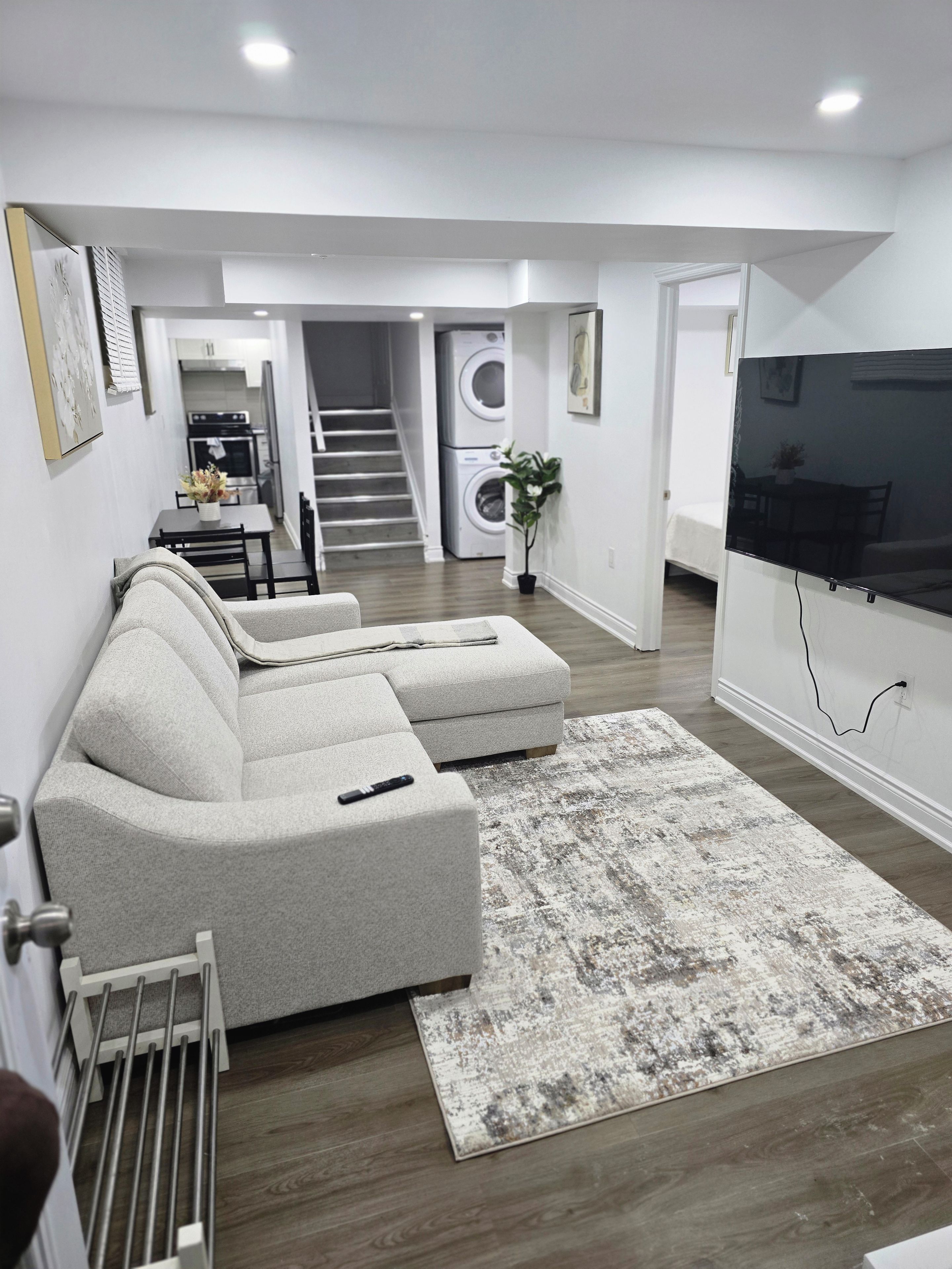 Ein modernes Wohnzimmer mit einer Eckcouch, einem Flachbildfernseher und einer Treppe zu einem Waschbereich.