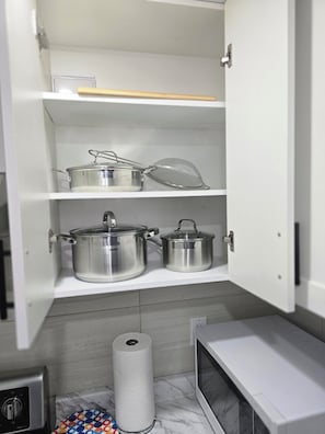 Eine Küche mit weißen Schränken, Edelstahlkochgeschirr, einem Sieb, einer Küchenpapierrolle und einer Mikrowelle.