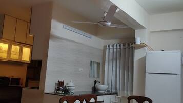 A compact kitchen with a dining area, a ceiling fan, and a refrigerator.