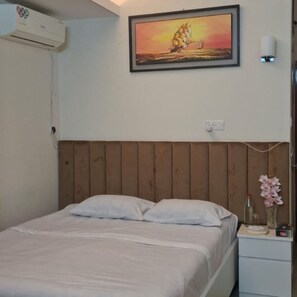 A bedroom with a wooden headboard, a bed with white bedding, a nightstand with a vase of flowers, and a painting of a sailboat on the wall. - Marvelous 2-bedroom apartment with AC in vibrant Dhaka (Dhaka)