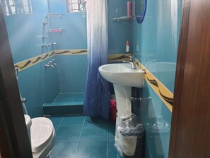 Et badeværelse med toilet, håndvask, bruser og blå fliser.