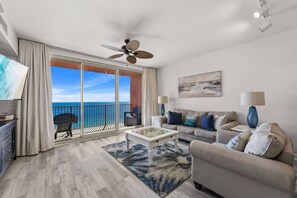 Ein geräumiges Wohnzimmer mit Balkon, Deckenventilator, einer Sofagarnitur und einem Flachbildfernseher.
