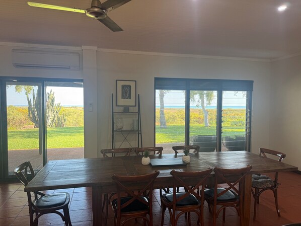 A dining area with a large table and chairs, a ceiling fan, and a view of a landscape through glass doors.