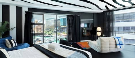 Una habitación de hotel moderna con una cama grande, una zona de estar, un televisor y vistas a la ciudad.