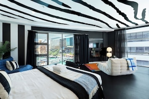 A modern hotel room with a large bed, a seating area, a TV, and a city view. - Boutique Designer Studio at Shed 19 (Auckland)