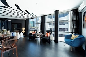 A modern living room with a large window, a blue armchair, and a dining area with a glass table. - Boutique Designer Studio at Shed 19 (Auckland)