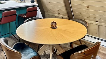 A round wooden table with four chairs, a decorative object on the table, and a kitchen area in the background.