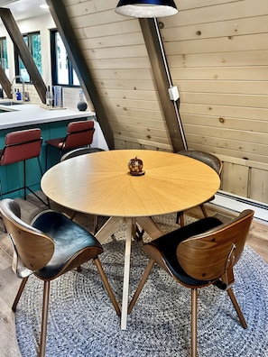 A round wooden table with four chairs, a decorative object on the table, and a kitchen area in the background. - 
Shaver Haus - Cozy A-Frame Retreat in the Pines of Shaver Lake (Shaver Lake)