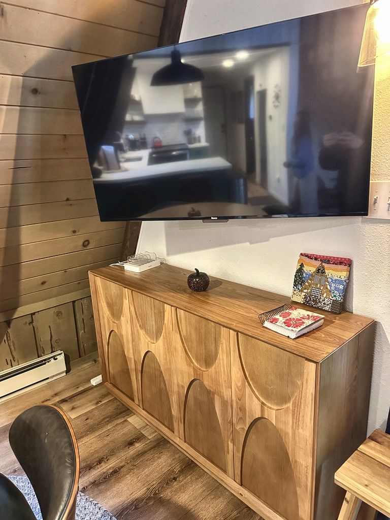 A room with a wooden cabinet, a flat-screen TV mounted on the wall, and a small table with a decorative item.