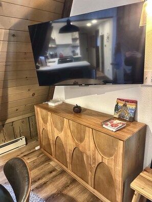 A room with a wooden cabinet, a flat-screen TV mounted on the wall, and a small table with a decorative item. - 
Shaver Haus - Cozy A-Frame Retreat in the Pines of Shaver Lake (Shaver Lake)