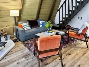 A cozy loft-style living room with a sofa, two armchairs, a coffee table, and a staircase. - 
Shaver Haus - Cozy A-Frame Retreat in the Pines of Shaver Lake (Shaver Lake)