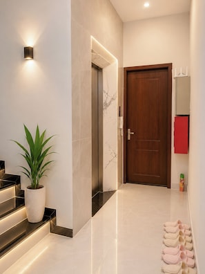 A modern hallway with a marble wall, a potted plant, a wooden door, and a row of slippers. - 4-bedroom house in tranquil Thành phố Hồ Chí Minh with AC (Thành phố Hồ Chí Minh)