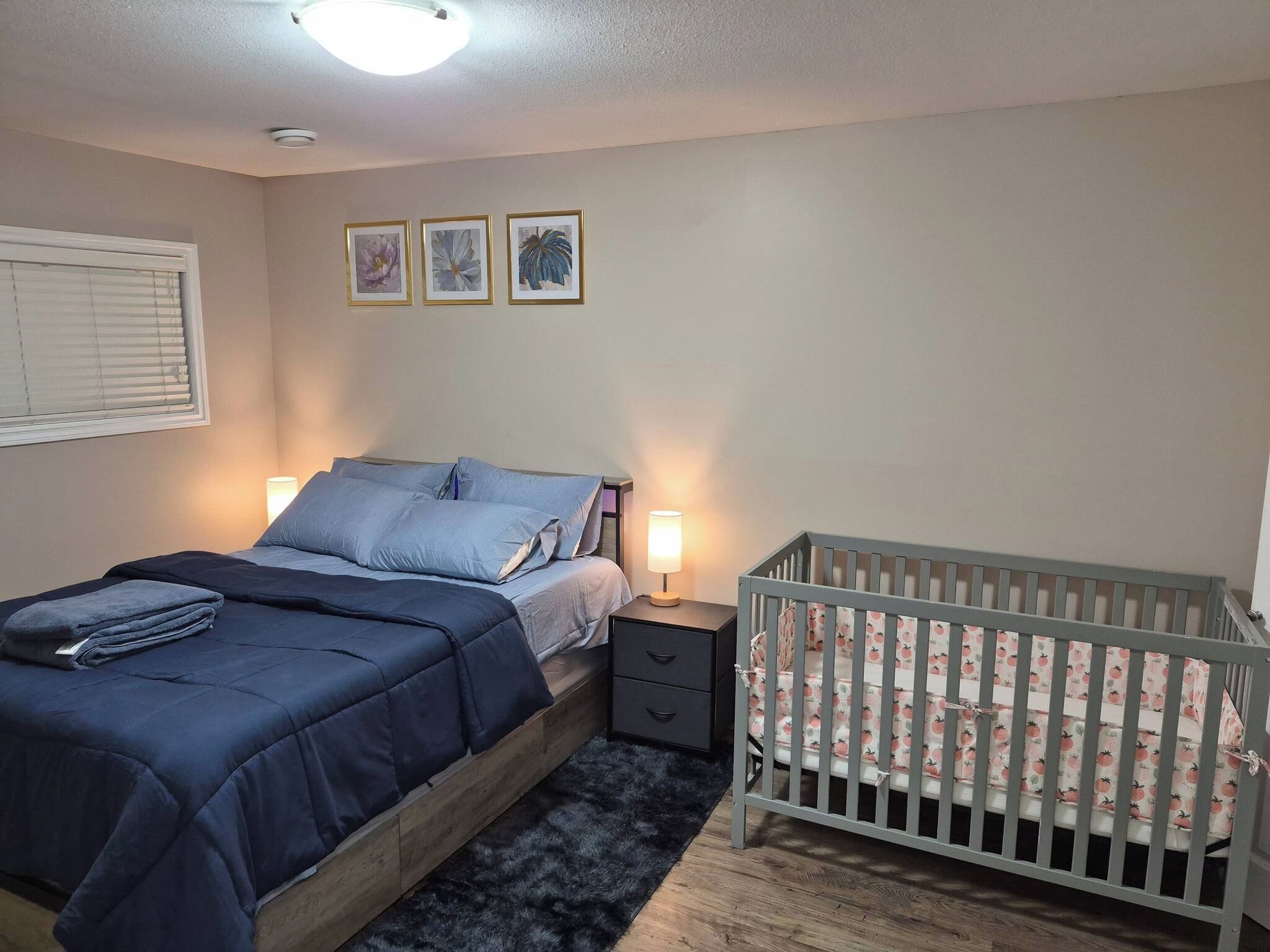 A bedroom with a bed, bedside tables, a crib, and wall-mounted artwork.
