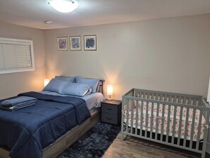 Un dormitorio con cama, mesitas de noche, cuna y una obra de arte en la pared.