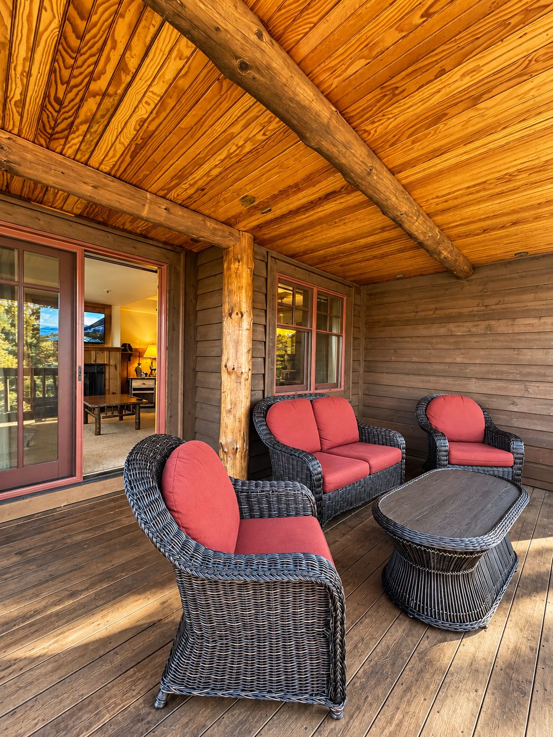 A covered outdoor seating area with wicker furniture and red cushions.