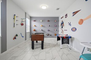 A room with a foosball table, sports memorabilia on the walls, and a window with blinds. - 6BR Villa Champions Gate Resort Prime Location (Four Corners)