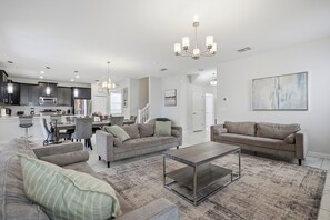 A modern living space with a kitchen, dining area, and seating area. - 6BR Villa Near Disney at Champions Gate Resort (Four Corners)